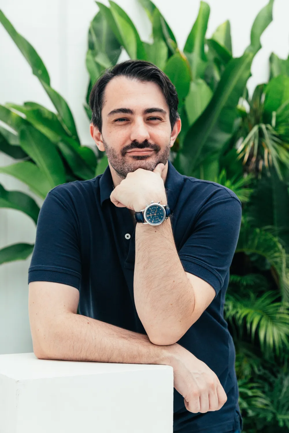 Vivien Roggero in a navy polo, leaning on a white plinth in front of tropical plants