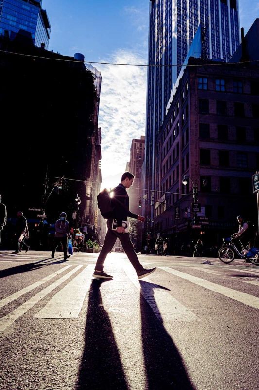 A Man Walking Across A Street Next To Tall Buildings